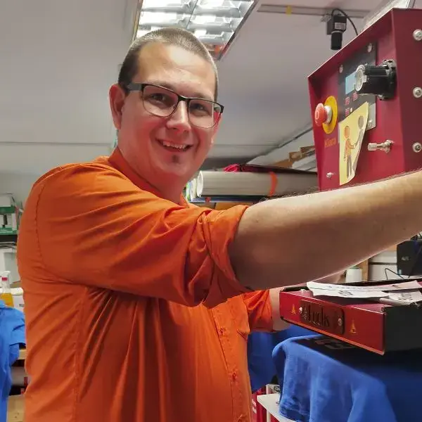 Mann mit orangem Hemd bedient eine Transferpresse